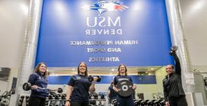 People posed with workout equipment in the gym below the MSU Denver's Human Performance and Sport Athletics sign.