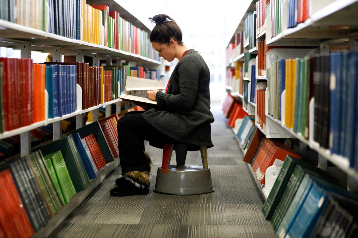 学生在图书馆两个书架之间看书