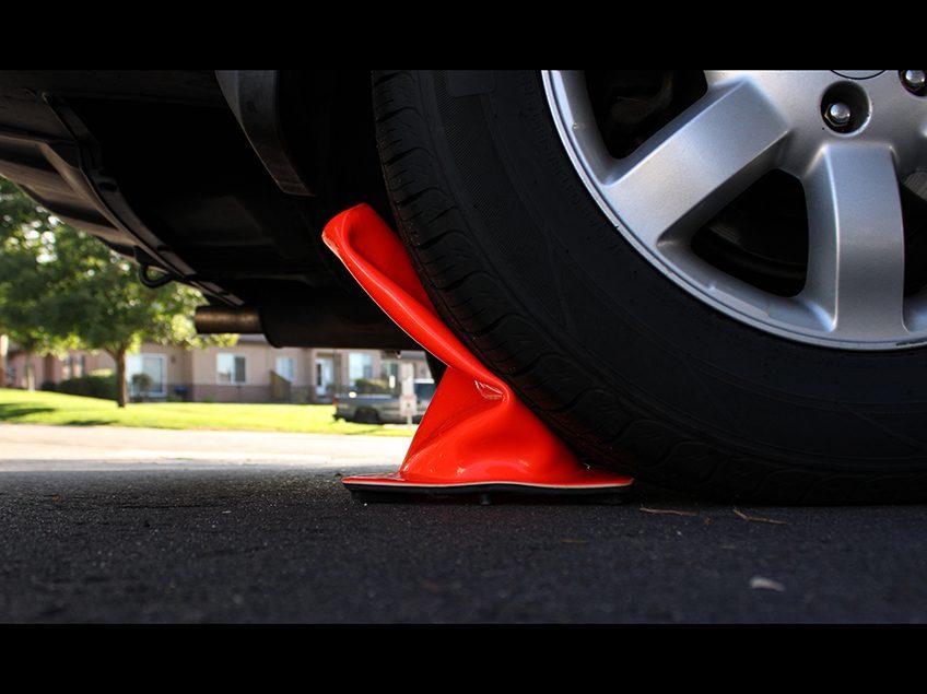 Close up of a car tire crushing an orange traffic cone.